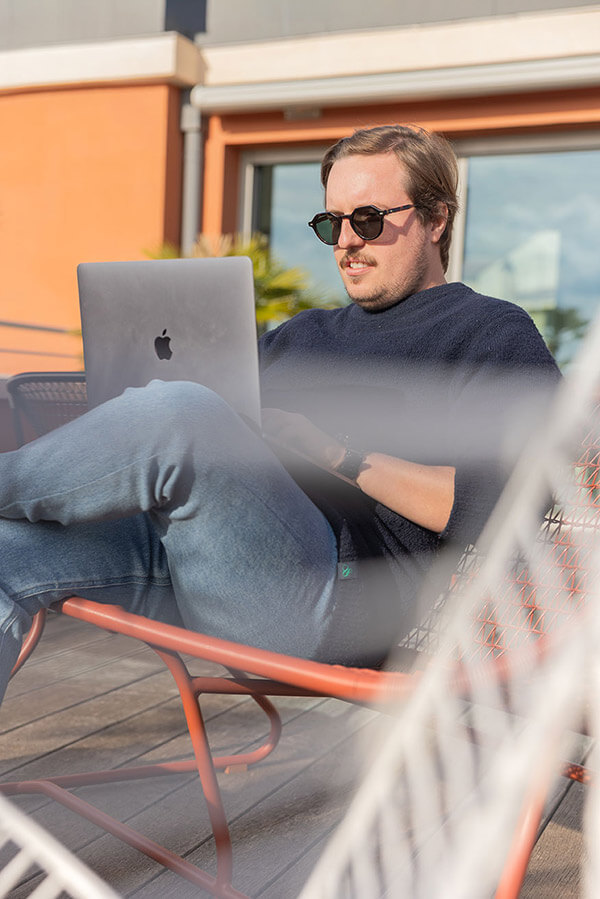 jeune homme qui travaille sur son ordinateur sur une terrasse au soleil